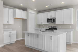 Kitchen featuring a kitchen island with sink, sink, white cabinets, and stainless steel appliances