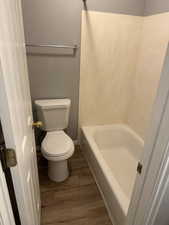 Bathroom with a tub to relax in, hardwood / wood-style floors, and toilet