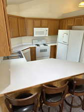 Kitchen with a kitchen bar, kitchen peninsula, sink, and white appliances