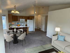 Kitchen featuring kitchen peninsula, white appliances, pendant lighting, an inviting chandelier, and lofted ceiling