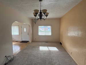 Interior space with a textured ceiling, light carpet, and a chandelier