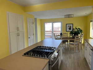 Kitchen featuring light hardwood / wood-style floors, a kitchen island, white cabinetry, and stainless steel gas range