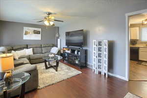 Living room featuring ceiling fan, dark wood-type flooring, and a textured ceiling