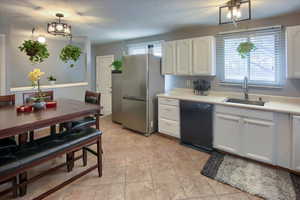 Kitchen with pendant lighting, dishwasher, white cabinets, sink, and stainless steel fridge