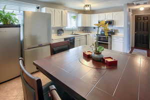 Kitchen with tile countertops, white cabinetry, sink, and appliances with stainless steel finishes