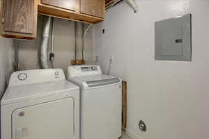 Laundry area featuring electric panel, washer and clothes dryer, and cabinets