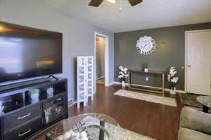 Living room with a textured ceiling, ceiling fan, and dark wood-type flooring