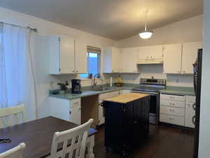 Kitchen with stainless steel range with electric cooktop, refrigerator, decorative light fixtures, a kitchen island, and white cabinetry