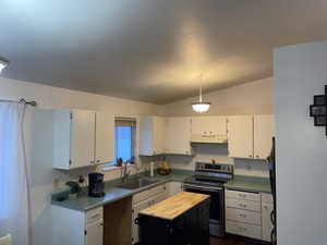 Kitchen with white cabinets, lofted ceiling, electric stove, and sink