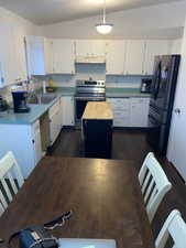 Kitchen with a center island, white cabinets, vaulted ceiling, dark hardwood / wood-style floors, and appliances with stainless steel finishes