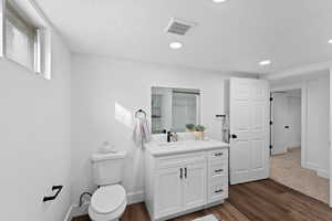 Bathroom with hardwood / wood-style floors, vanity, toilet, and a textured ceiling