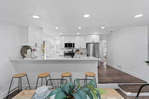 Kitchen featuring sink, white cabinetry, dark hardwood / wood-style flooring, kitchen peninsula, and stainless steel appliances