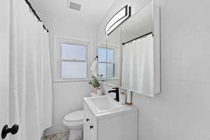 Bathroom with a textured ceiling, vanity, tile walls, and toilet