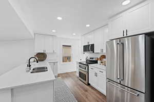 Kitchen with light stone countertops, sink, appliances with stainless steel finishes, white cabinets, and light wood-type flooring