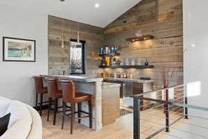 Bar featuring wooden walls, high vaulted ceiling, and light wood-type flooring