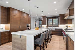 Kitchen with light hardwood / wood-style floors, a kitchen island with sink, stainless steel appliances, and hanging light fixtures