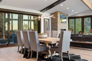 Dining area featuring vaulted ceiling with beams, light wood-type flooring, a fireplace, and a chandelier