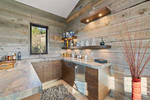 Bar featuring wood walls, lofted ceiling, sink, light hardwood / wood-style flooring, and stainless steel fridge