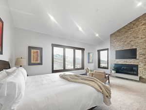 Carpeted bedroom featuring vaulted ceiling and a stone fireplace