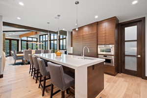 Kitchen featuring light wood-type flooring, sink, decorative light fixtures, a center island with sink, and a breakfast bar area