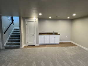 Bar with white cabinets, light colored carpet, and sink