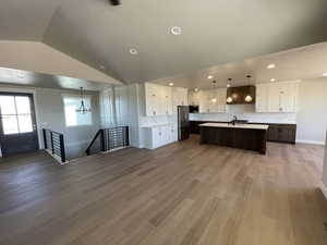 Kitchen featuring stainless steel fridge, premium range hood, wood-type flooring, lofted ceiling, and an island with sink