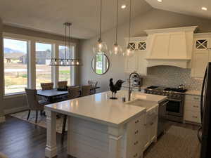 Kitchen with white cabinets, a center island with sink, stainless steel appliances, and premium range hood