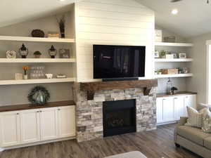 Living room featuring dark hardwood / wood-style floors, vaulted ceiling, and a stone fireplace