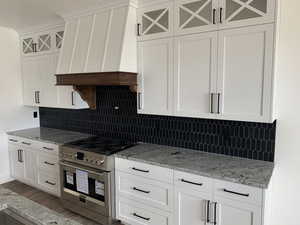 Kitchen featuring tasteful backsplash, light stone counters, high end stove, hardwood / wood-style floors, and white cabinetry