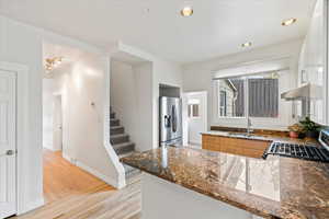 Kitchen featuring granite countertops, kitchen peninsula, stainless steel appliances, with view into laundry room and of stairs leading to master suite