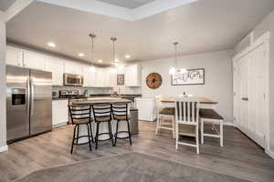 Kitchen with white cabinetry, hanging light fixtures, a chandelier, wood-type flooring, and appliances with stainless steel finishes