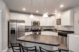 Kitchen featuring appliances with stainless steel finishes, sink, white cabinets, light hardwood / wood-style floors, and hanging light fixtures