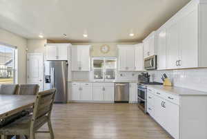 Kitchen featuring white cabinets, appliances with stainless steel finishes, tasteful backsplash, and light hardwood / wood-style flooring