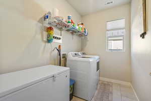 Clothes washing area featuring washer and dryer and light tile patterned floors