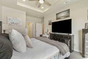 Bedroom with light colored carpet, ceiling fan, and a tray ceiling