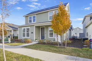 View of front of home featuring a front lawn, cooling unit, and solar panels