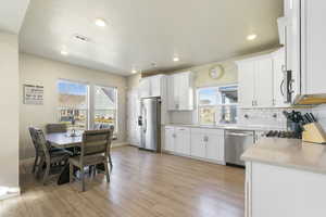 Kitchen with white cabinets, a healthy amount of sunlight, appliances with stainless steel finishes, and light hardwood / wood-style flooring