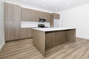 Kitchen featuring sink, stainless steel appliances, light stone counters, light hardwood / wood-style flooring, and an island with sink