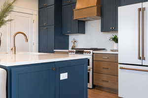 Kitchen featuring high quality appliances, premium range hood, sink, light wood-type flooring, and tasteful backsplash