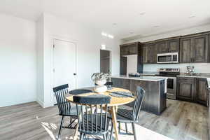 Kitchen with light wood-type flooring, stainless steel appliances, a kitchen island, and light stone countertops