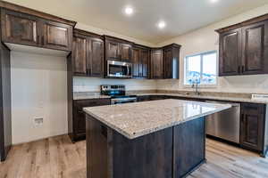 Kitchen featuring light stone countertops, stainless steel appliances, sink, a center island, and light hardwood / wood-style floors