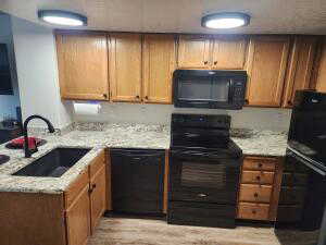 Kitchen featuring sink, light granite counters, light hardwood / wood-style flooring, kitchen peninsula, and black appliances