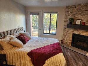 Bedroom with access to outside, a stone fireplace, and wood-type flooring