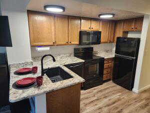 Kitchen featuring sink, light granite counters, light hardwood / wood-style flooring, kitchen peninsula, and black appliances