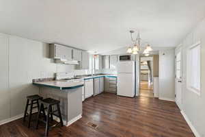 Kitchen with kitchen peninsula, white appliances, vaulted ceiling, dark wood-type flooring, and hanging light fixtures