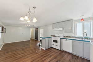 Kitchen with white appliances, sink, a notable chandelier, dark hardwood / wood-style floors, and hanging light fixtures