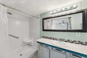 Bathroom with ceiling fan, vanity, a textured ceiling, and walk in shower