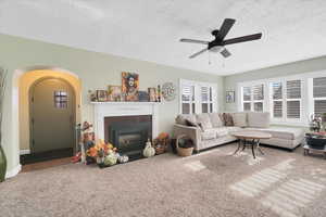 Carpeted living room with ceiling fan, a fireplace, and a textured ceiling