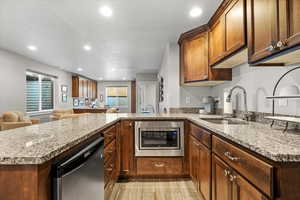 Kitchen with kitchen peninsula, appliances with stainless steel finishes, light wood-type flooring, light stone countertops, and sink