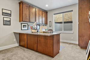 Kitchen with light stone counters, kitchen peninsula, and light carpet